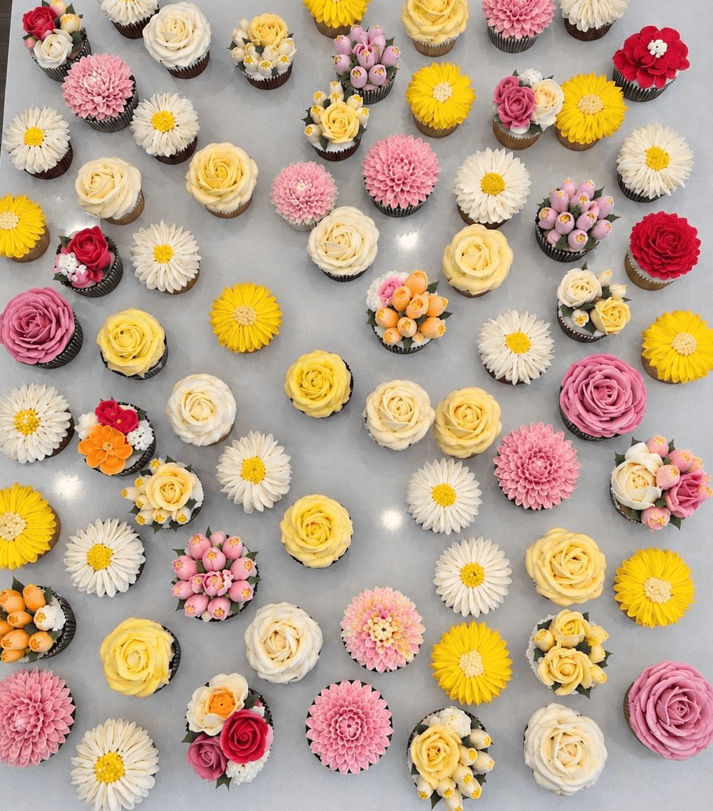 A spread of hand-piped buttercream flower cupcakes in yellow, pink, red and cream
